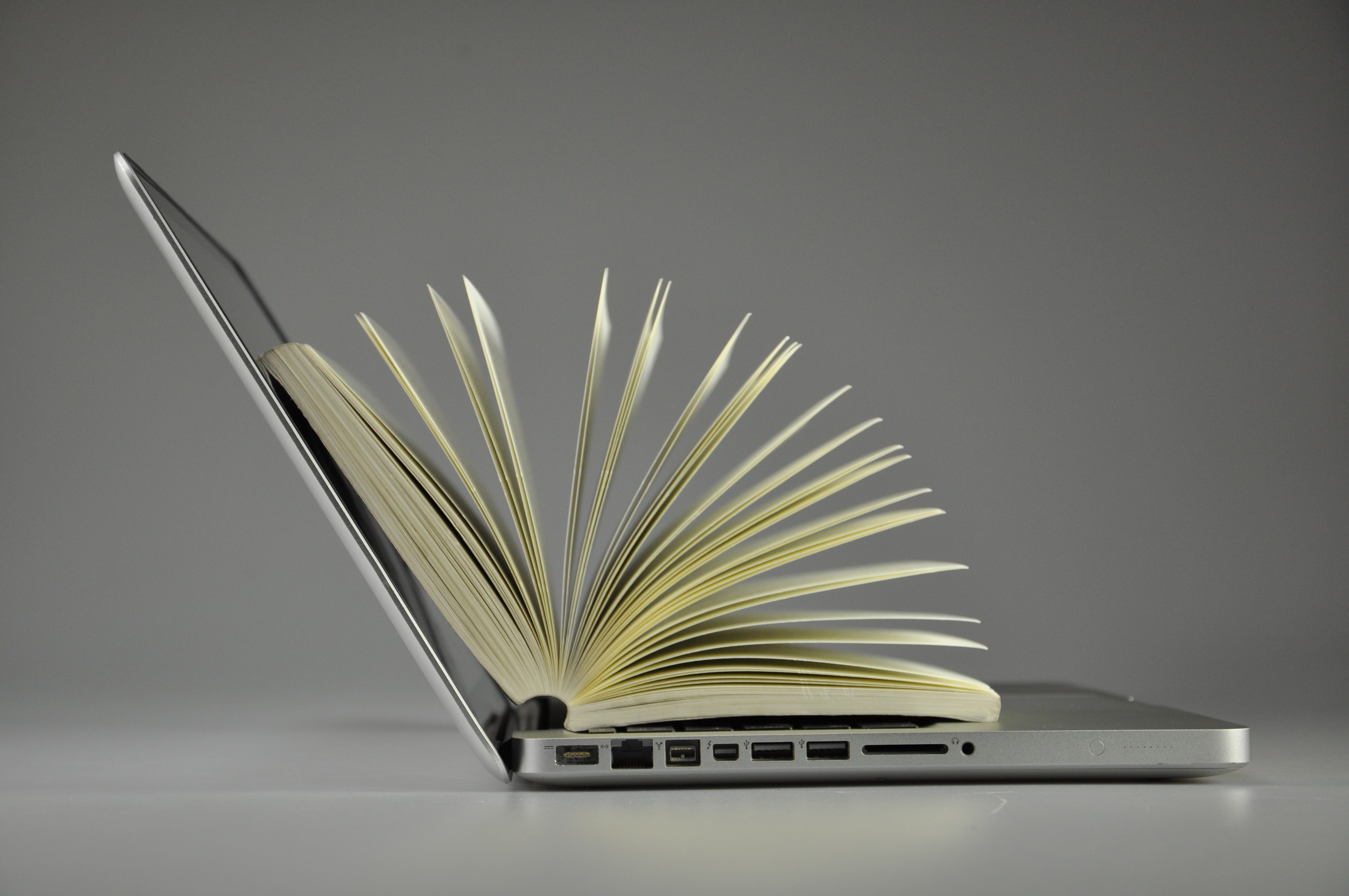 Livro com páginas abertas apoiado como se estivesse saindo do notebook.