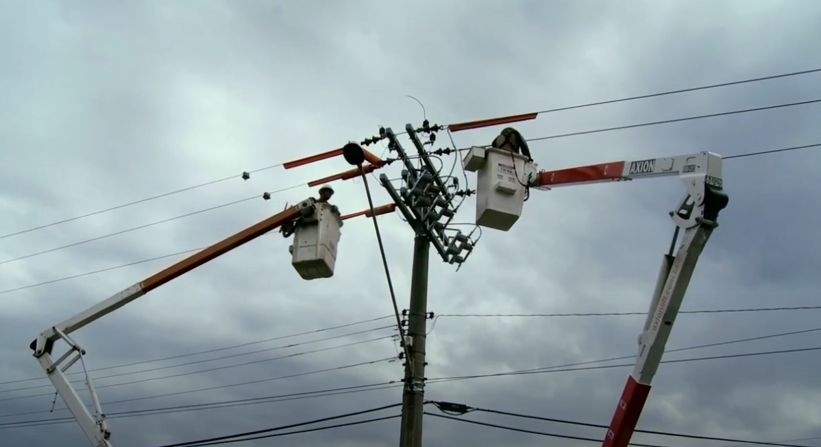 Imagem com poste de liuz e pessoas trabalhando suspensas, do filme "Eletricitários". 