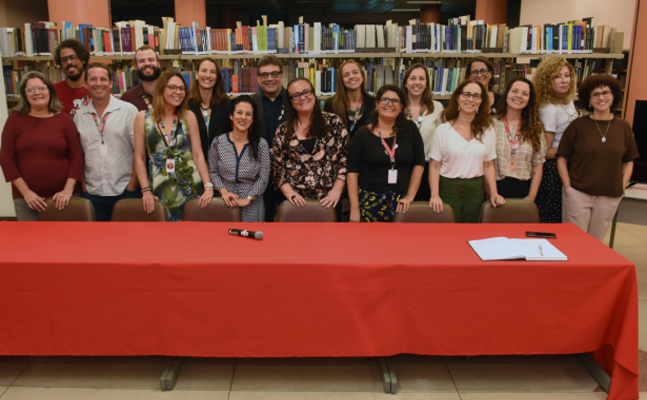 Foto da diretoria e chefias eleitas tendo uma mesa em frente e as estantes da biblioteca ao fundo