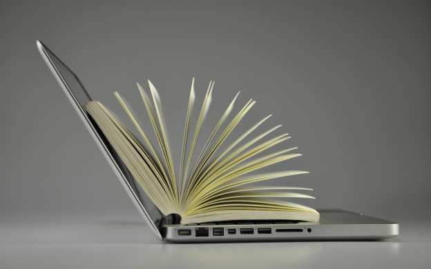 Livro com páginas abertas apoiado como se estivesse saindo do notebook.