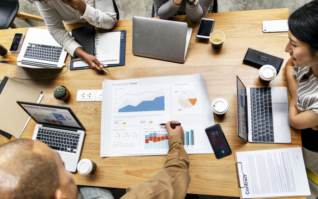 grupo de pessoas reunidadas, em debate, com computadores e materiais de trabalho.