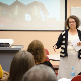 Pesquisadora Claudia Travassos, branca, cabelos escuros, óculos vermelhos, em sala de aula, blusa branca, casaco branco e preto. Foto: Raquel Portugal/Fiocruz Imagens.