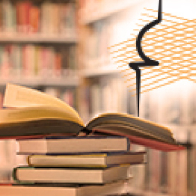 Foto de vários livros empilhados, sendo que o de cima está aberto e, no fundo, imagem de uma estante com livros.