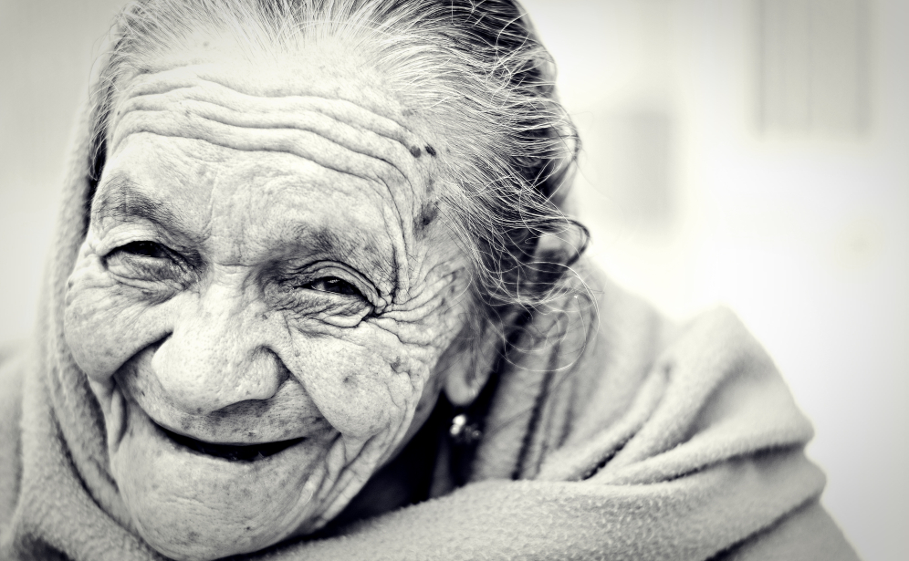 Foto do rosto de mulher idosa sorridente, em preto e branco