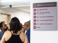 Foto de placa nas instalações do PPGICS com alunos conversando ao fundo. Foto: Raquel Portugal