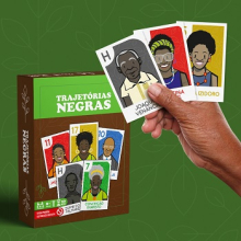 Capa do jogo com cartões de celebridades negras em um fundo verde, ao lado de uma mão negra segurando 3 cartas de pessoas negras do jogo.