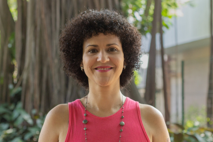 Pesquisadora Irene Kalil, branca, cabelos cacheados pretos, blusa rosa, com árvore ao fundo. Foto: Raquel Portugal/Fioruz Imagens.
